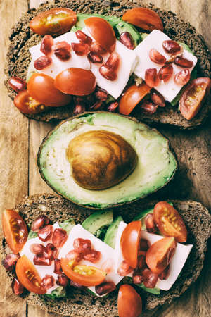 Two slices of bread with avocado, fresh cheese and cherry tomatoes, separated by an avocado.