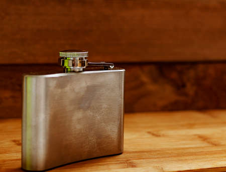 Liquor flask made of metal on a wooden background.の写真素材