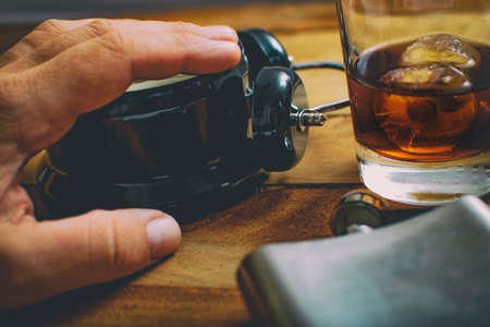 Alcoholism concept. Hand on an alarm clock with a glass of whiskey and a flask next to it.
