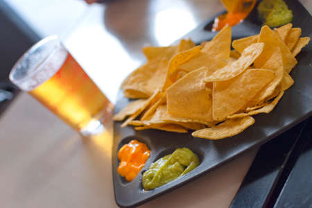Mexican nachos dish with guacamole sauce and cheese sauce. With accompaniment of beer and chips.の写真素材