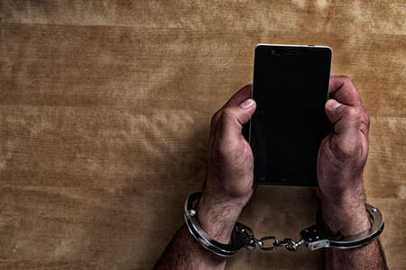 Crime concept in the network. Shaking hands holding a mobile phone.の写真素材