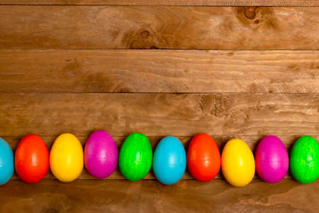 Easter eggs in line, colored: yellow, pink, green, blue and orange, on a wooden table.の写真素材
