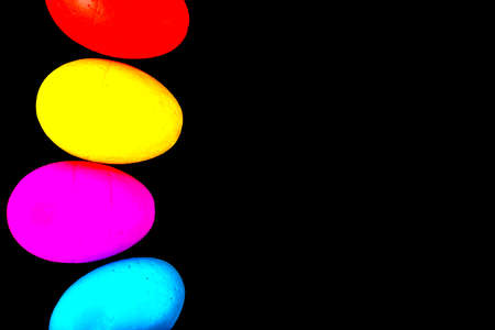 Easter eggs of blue, yellow, orange and green color, on a black background.