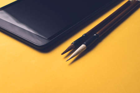 Tablet next to two writing brushes of Chinese characters (Mao Pi), on a yellow background.の写真素材
