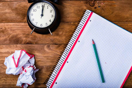 Green pencil on checkered paper background with alarm clock, concept time to be creative.
