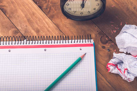 Green pencil on checkered paper background with alarm clock, concept time to be creative.