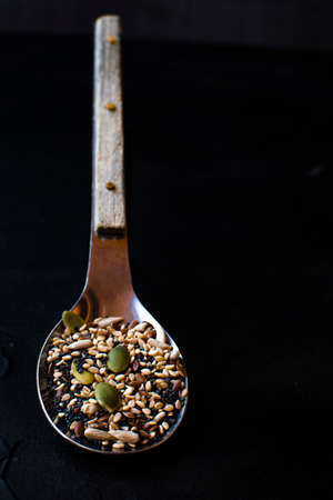 Sesame seeds next to different fruit seeds on a wooden spoon. Dark food concept.の写真素材