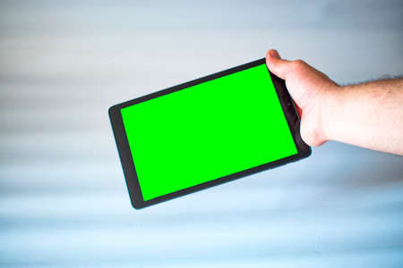Green screen. Tablet with green screen fastened with one hand on white background.の写真素材