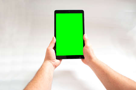 Green screen. Tablet with green screen fastened with two hands on white background.の写真素材