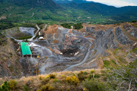 Stone quarry located at the bottom of a hillside between mountains and green meadows.