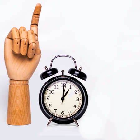 Wooden hand raising a finger, next to a clock marking the one.の写真素材