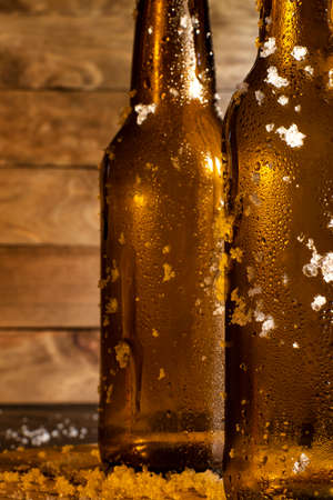 Two bottles of ice cold beer fresh out of the fridge, with a rustic wooden background.の写真素材