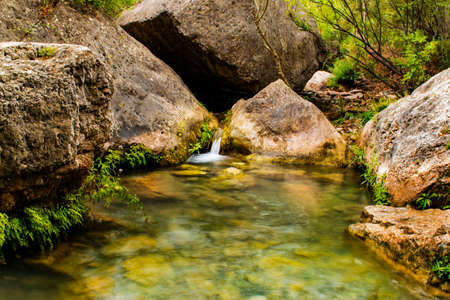 Small waterfall coming out of two large rocks and flowing into a river between the vegetation.の写真素材