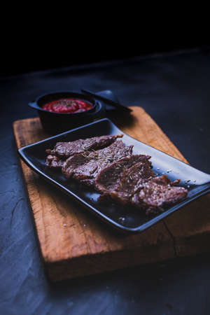 Sliced grilled beef steak. Beef steak with tomato sauce on the cutting board on dark wooden background.の写真素材