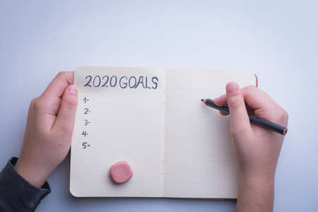 New Year 2020 target, action text in notepad with woman's hands and white background.の写真素材