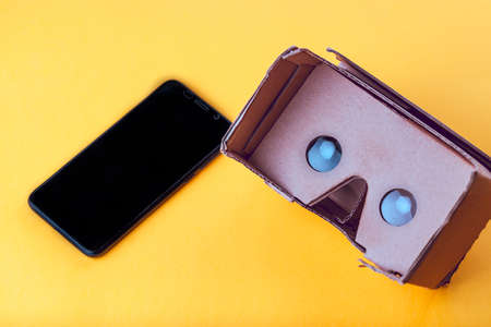 Cardboard virtual reality glasses with mobile phone on a yellow background