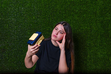 Girl with a thoughtful face in a black T-shirt with virtual reality glasses and a green background