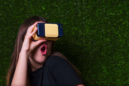 Surprised girl with black T-shirt looking with virtual reality glasses and green background