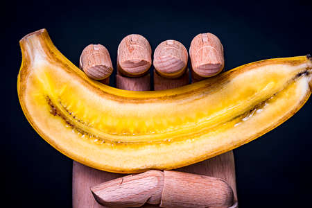 Wooden hand holding a banana split in half with black background.の写真素材