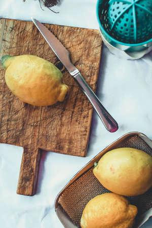 Freshly picked lemons on a wooden cutting board with a silver knife.