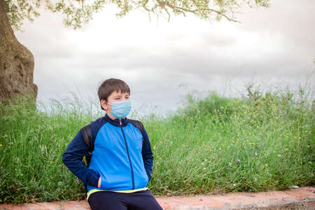 Boy with sportswear and backpack with field in the background taking a walk, with the mask on.