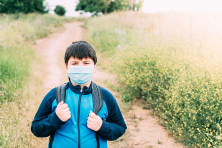 Boy with backpack and blue jacket prepared to go to school with the mask on his face.の写真素材