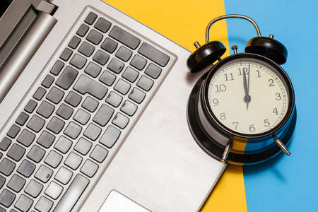 Alarm clock with a laptop on a yellow and blue background.の写真素材