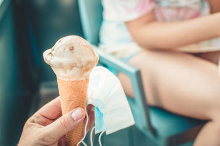 New normality concept. Person holding an ice cream in his hand while holding a mask.