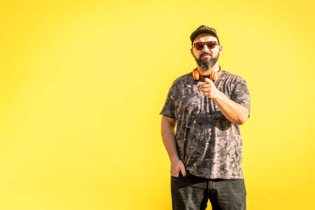 Curvy man with cap, sunglasses pointing forward with yellow background.の写真素材