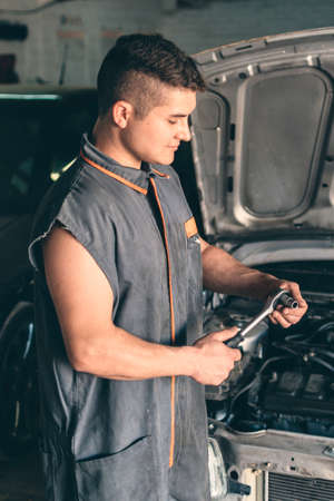 Mechanic looking at a ratchet wrench with the hood of an open car in the background.