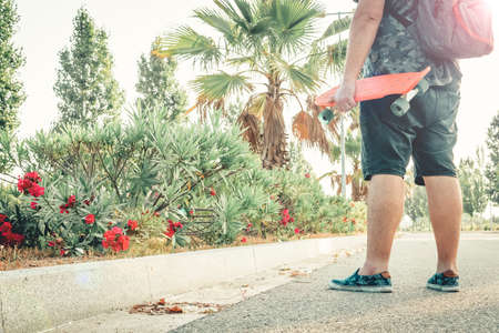 Curvy man holding an orange skateboard on the road.の写真素材