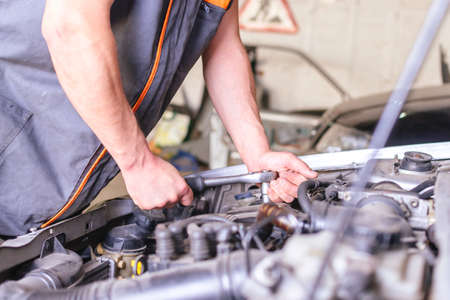 Mechanic in overalls working with a wrench on the car engine.