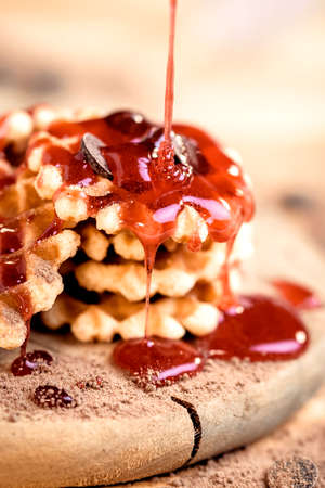 Close-up of mini waffles with strawberry syrup and chocolate shavings.