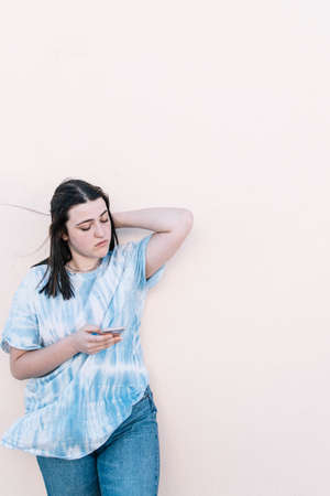 Teen girl in a tie dye shirt on a pinched orange wall looking at the smartphone