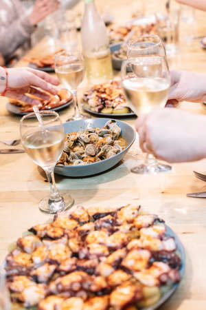Table full of seafood dishes and glasses with people toasting white wine.の写真素材