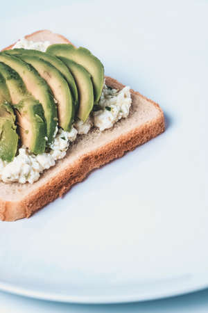 Close-up of a slice with cheese and avocado on a white plate.の写真素材