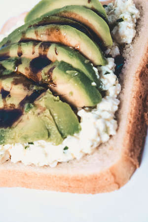 Close-up of a slice with cheese and avocado on a white plate.の写真素材
