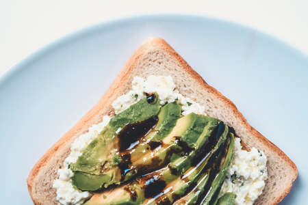 Slice of bread with fresh cheese and avocado cut on top.の写真素材