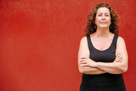 Woman with curly hair looking at camera with arms crossedの写真素材