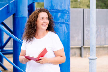 Woman with curly hair waiting for someone with a book.の写真素材