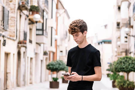 Teen boy with curly hair looking at the phoneの写真素材