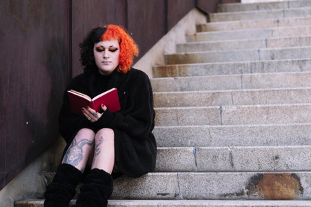 Trans girl reading a red book on some stairs.の写真素材