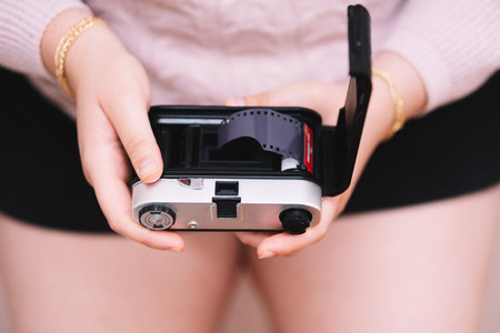 Girl in a pink sweater putting film on a photo camera.の写真素材