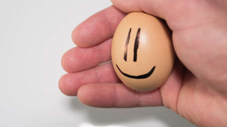chicken egg with a smiley in a man's handの写真素材