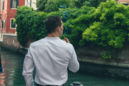 guy in a shirt smokes a cigarette on the street near the river in Veniceの写真素材