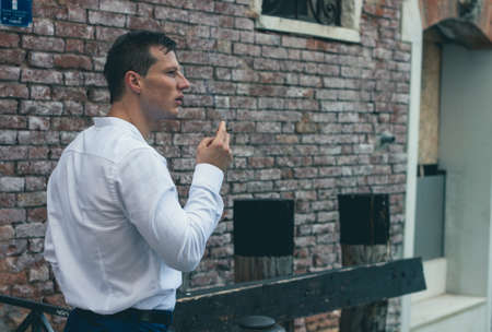 handsome young guy in a white shirt holds a cigarette in his handの写真素材