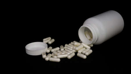 Medical pills on a black background with a white empty bottleの写真素材