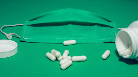 Medical mask, scattered tablets in capsules, vitamins, therapeutic, healthy lifestyle, on a greenの写真素材