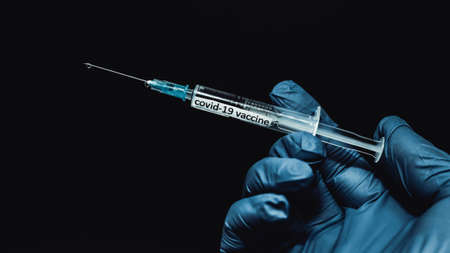 A syringe with a vaccine, a drop of medicine flows down the needle, a hand in a medical glove holds a syringe with a vaccine against covid-19, close-up.の写真素材