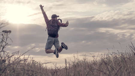 Happy guy in a jump in the field, in nature, a young man jumped beautifully at sunset, a cheerful man enjoying nature and the landscape at sunrise.の写真素材